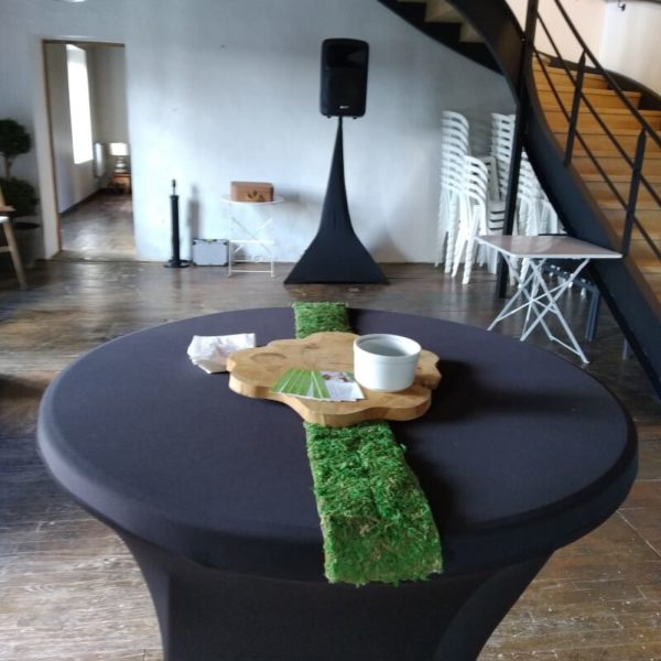 Table cocktail mange debout noir dans une salle des fêtes lors d'un événement avec une enceinte et des chaises en arrière plan