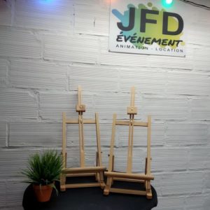 2 petits chevalets en bois pliables installés sur une table noire devant un mur blanc et sous des guirlandes guinguette