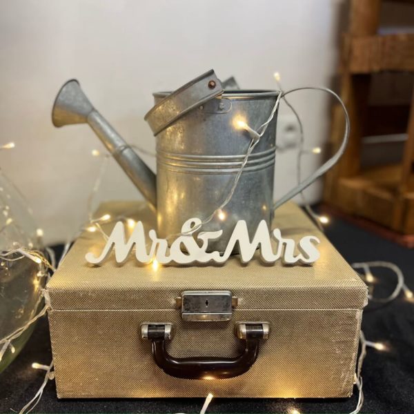 Joli arrosoir en métal sur une valise vintage avec des guirlande leds et des lettres Mrs & Mrs en bois